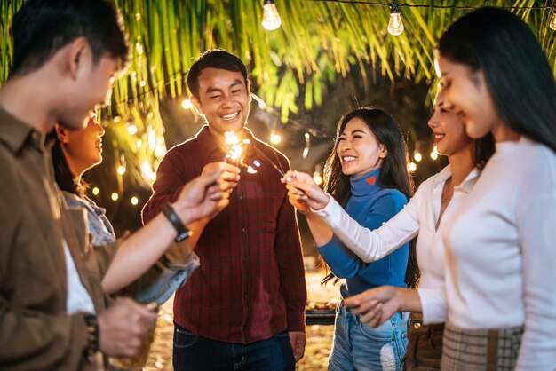 Portrait of Happy Asian group of friends having fun with sparklers outdoor Young people having fun with fireworks at night time People food drink lifestyle new year celebration concept