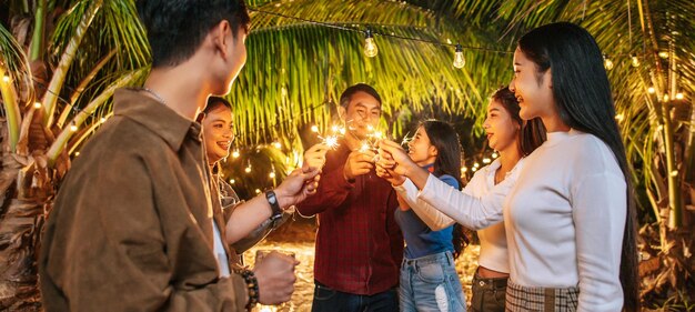 Portrait of Happy Asian group of friends having fun with sparklers outdoor Young people having fun with fireworks at night time People food drink lifestyle new year celebration concept