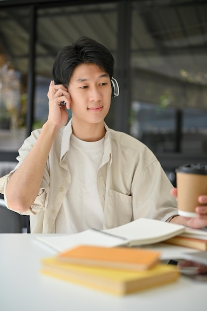 Portrait of happy Asian man listening to music through headphones while relaxing in the cafe