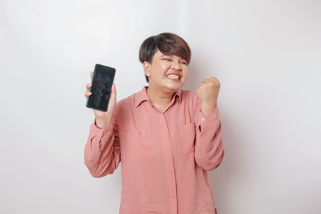 A portrait of a happy Asian woman is smiling and showing copy space on her smartphone wearing pink shirt isolated by a white background