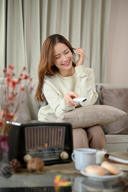 Portrait Happy Asian woman on the sofa in her living room enjoying watching a TV shows or movie