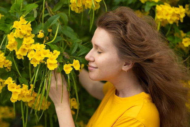 Portrait of happy beautiful bearded girl young positive woman with beard is smelling beautiful yellow flowers in the garden smiling enjoying spring or summer day breathing deep deeply fresh air