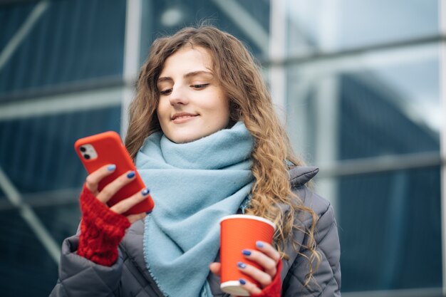 Portrait of happy beautiful curly woman with coffee cup takeaway use mobile phone texting messages.