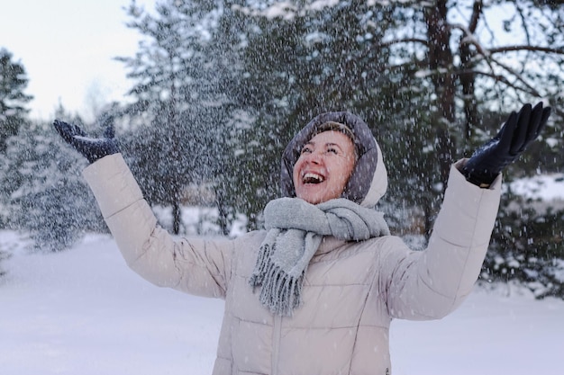 Portrait of happy beautiful elderly senior retired woman in age is playing having fun with snow outdoors in forest or park at winter cold day smiling enjoy weather