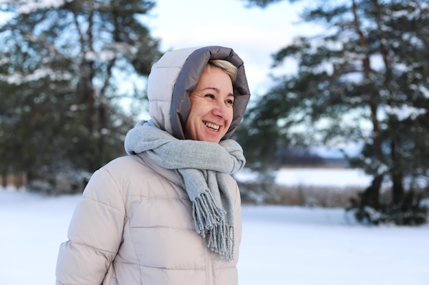 Portrait of happy beautiful elderly senior retired woman in age is playing having fun with snow outdoors in forest or park at winter cold day smiling enjoy weather