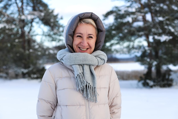 Portrait of happy beautiful elderly senior retired woman in age is playing having fun with snow outdoors in forest or park at winter cold day smiling enjoy weather