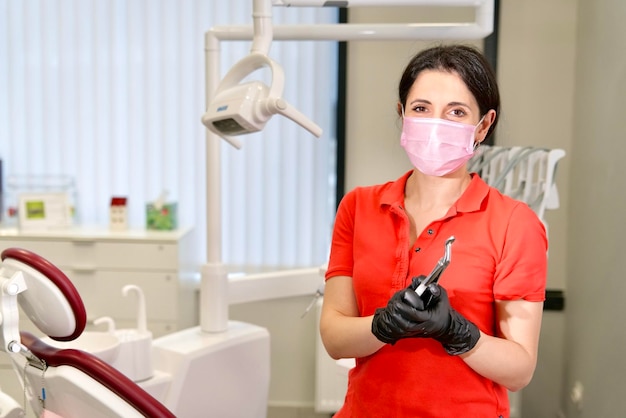 Portrait of happy beautiful female doctor attractive pretty middle aged Caucasian Armenian ethnic dentist in red polo standing in dental office at clinic smiling looking at camera