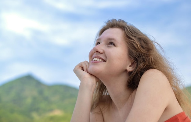 Portrait of happy beautiful young girl dreams and meditation relax nature tanning on sun at summer sunny day on natural background with sky and mountains breathing deep fresh air