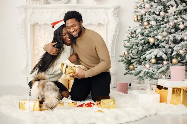 Portrait of happy black couple holding gifts and sitting near Christmas tree