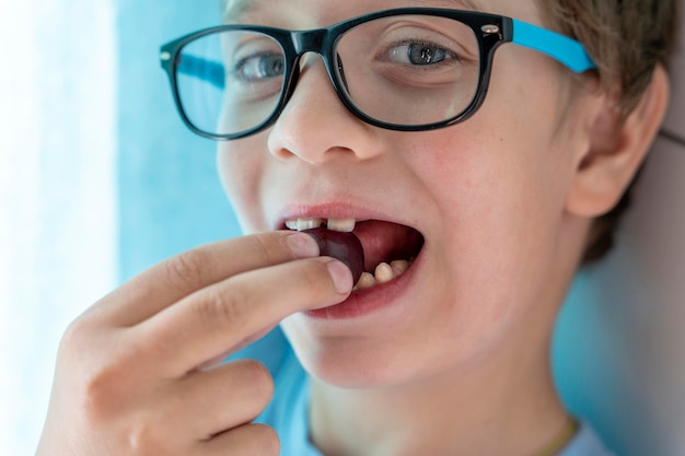 Portrait of a happy boy with glasses who eats cherries and smiles A cheerful child at home among the family Happy carefree childhood