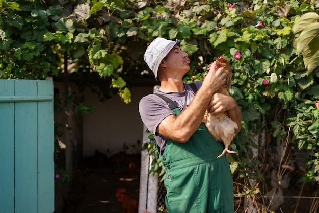 Portrait of happy caucasian farmer holding a brown hen outdoor Smiling mature man with chicken in hand with copy space