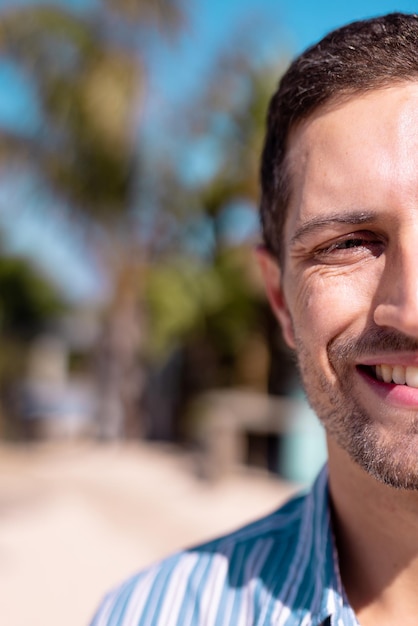 Portrait of happy caucasian man looking at camera and smiling at beach, with copy space. Spending quality time, lifestyle, summertime and vacation concept.