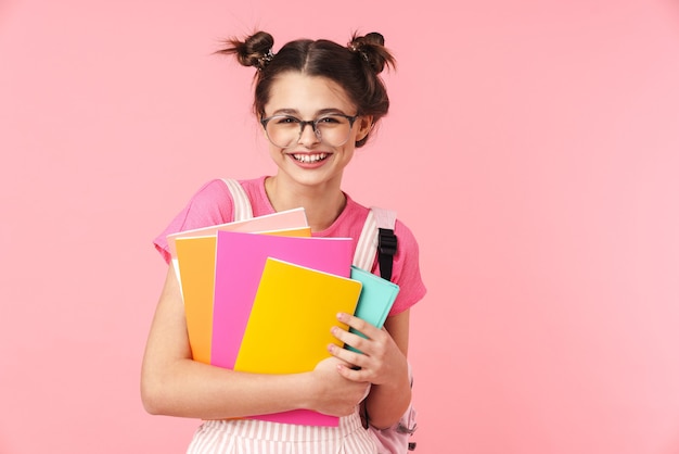 Portrait of happy charming girl posing with exercise books and smiling isolated over pink wall