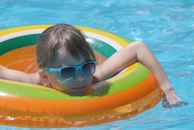 Portrait of happy child girl relaxing in inflatable circle in swimming pool on sunny summer day during tropical vacations Summertime activities concept