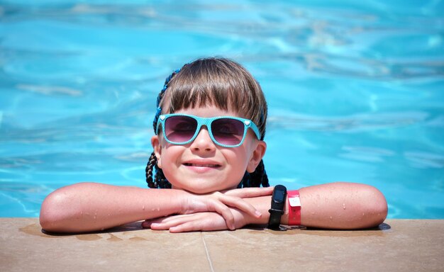 Portrait of happy child girl relaxing on swimming pool side on sunny summer day during tropical holidays