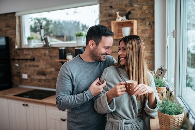 Portrait of a happy couple drinking coffee in the morning in the kitchen at home.