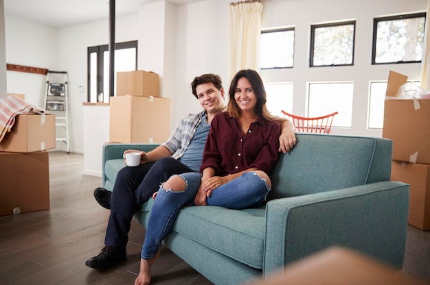 Portrait Of Happy Couple Resting On Sofa Surrounded By Boxes In New Home On Moving Day