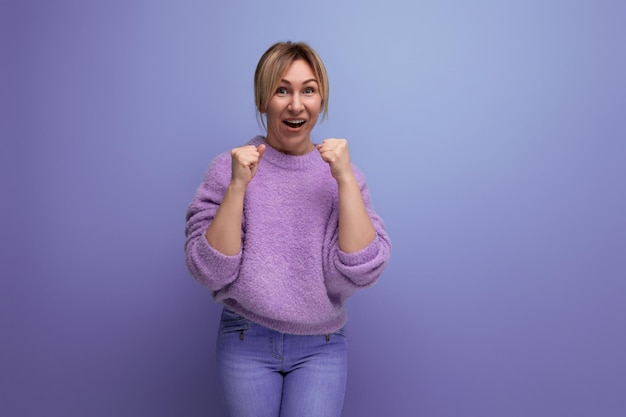 Portrait of a happy cute pleasant blond young woman in a lavender sweater who won on a bright plain