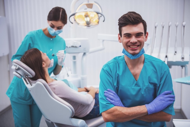 Portrait of a happy dentist in a mask and gloves on the background of the assistant who treats teeth patient