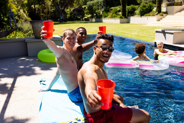 Portrait of happy diverse group of friends having pool party, holding plastic cups in garden. Lifestyle, friendship, party and summer.