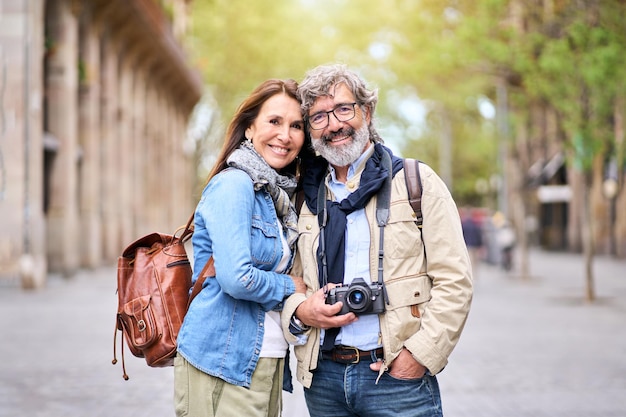 Portrait of happy elderly tourist couple posing for photo outdoors in city smiling senior people