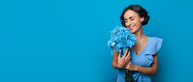 The portrait of a happy excited gorgeous young woman in an elegant blue dress is posing with a fresh bunch of blue flowers Mothers day Women's holidays Springtime Women rights