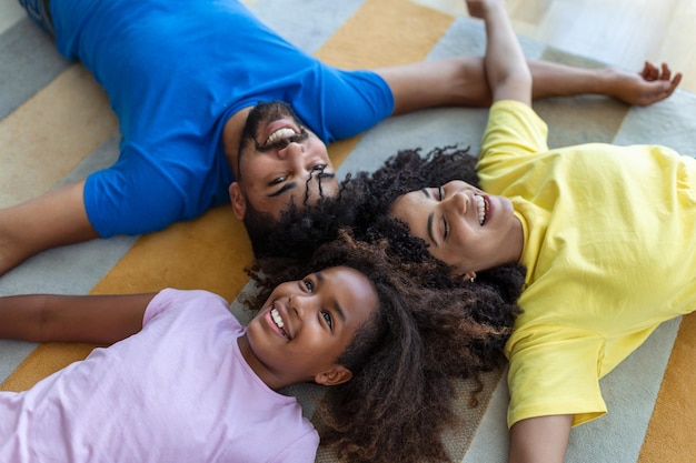 Portrait of happy family posing on floor at home laying on carpet and bonding cheerfully smiling view above Positive father mother and daughter cuddling top view