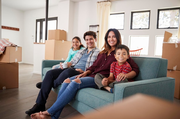 Portrait Of Happy Family Resting On Sofa Surrounded By Boxes In New Home On Moving Day