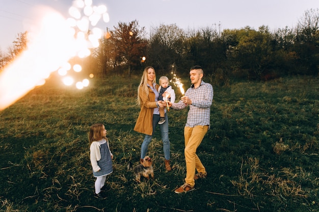 Portrait of a happy family with Bengal lights in a green field at sunset