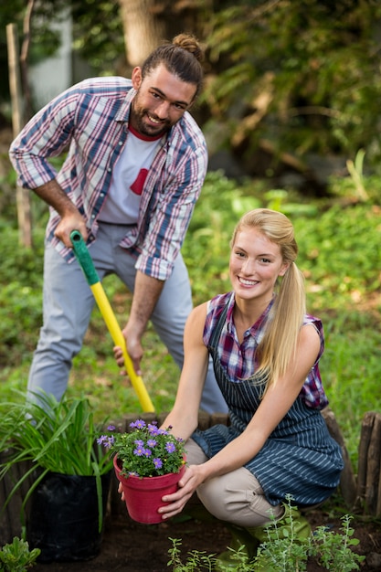 Portrait of happy gardeners with potted plant and shovel at garden