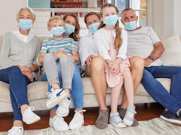 Portrait of happy generational caucasian family wearing face masks while relaxing on sofa at home Kids parents and grandparents staying responsible and safe from ill health during covid pandemic