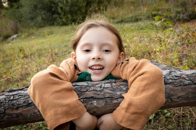 Portrait of a happy girl 6 years old hanging on a tree branch in the wild