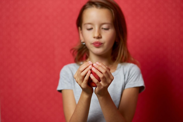 Portrait happy girl eats a peach on a red background