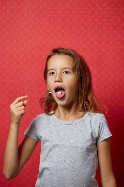 Portrait happy girl take capsule pill on her tongue on red background