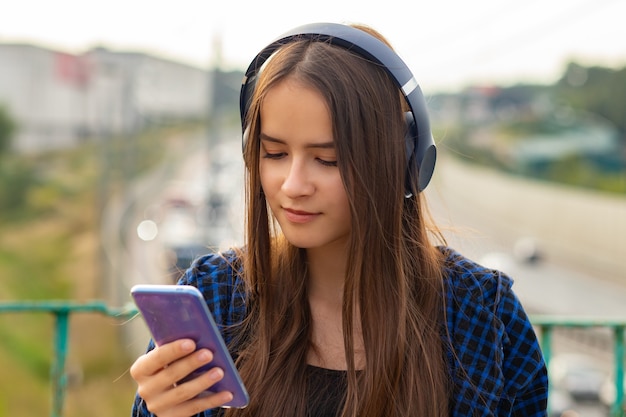 Portrait of a happy girl in wireless headphones in summer on a city street on a Sunny day