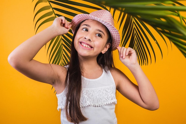 Portrait of happy girl with hat and palm leaves on yellow background.