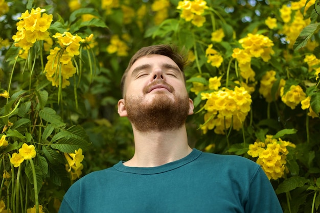 Portrait of happy handsome bearded guy young positive man with beard is smelling beautiful yellow