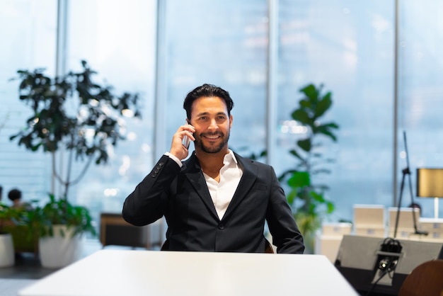 Portrait of happy handsome Hispanic businessman at coffee shop smiling and talking on phone