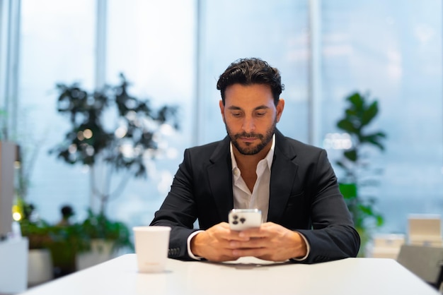 Portrait of happy handsome Hispanic businessman at coffee shop texting with phone