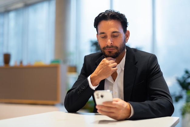 Portrait of happy handsome Hispanic businessman at coffee shop thinking and using phone