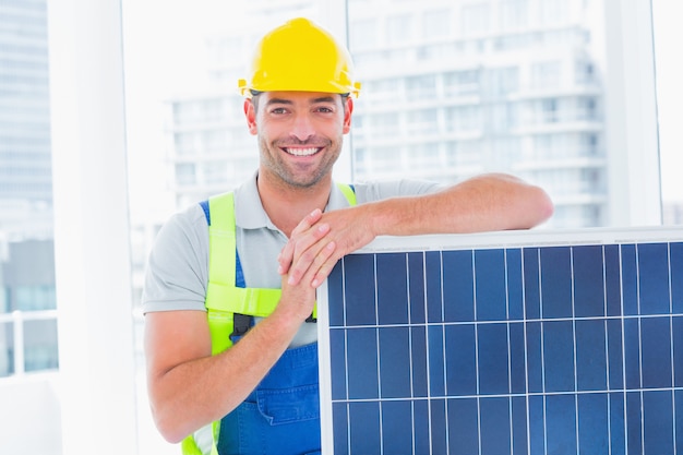 Portrait of happy handyman with solar panel in bright office