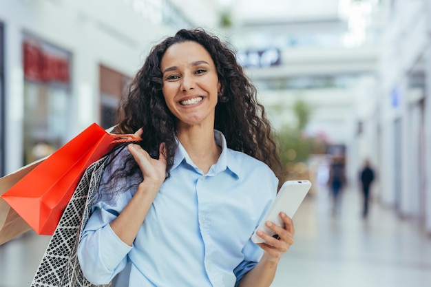 Portrait of happy hispanic woman shopper in store looking at camera and smiling holding colorful