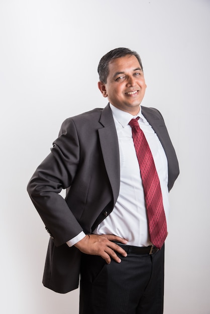 Portrait of happy Indian or Asian mid aged businessman in black suit with success sign while standing isolated over white background