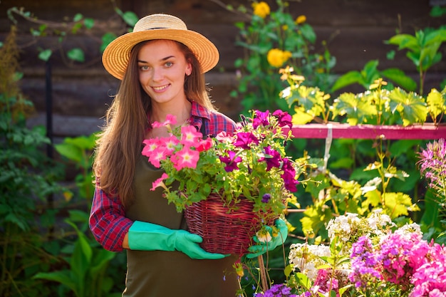 Portrait of happy joyful florist gardener woman in hat with flower pot of petunia outdoors. Gardening and floriculture. Growing flower in home garden