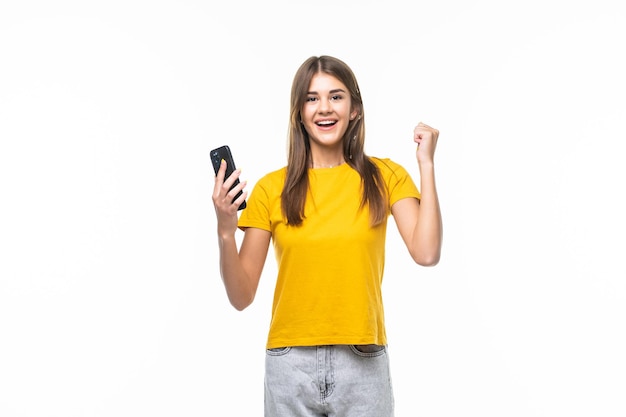 Portrait of a happy joyful girl holding mobile phone and celebrating a win isolated on white