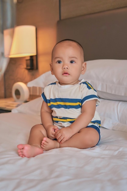 Portrait of happy little 6 month old Asian baby boy sitting on bed at home