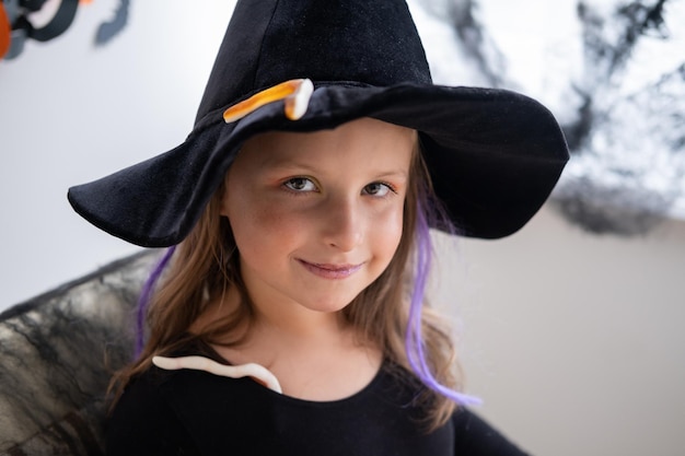 portrait of happy little girl in black witch hat at home celebrating Halloween