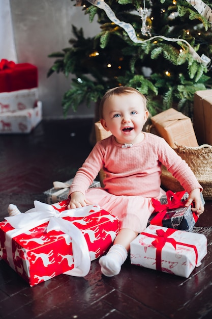 Portrait of happy little girl sitting on roof in decorated room and playing with Christmas presents.