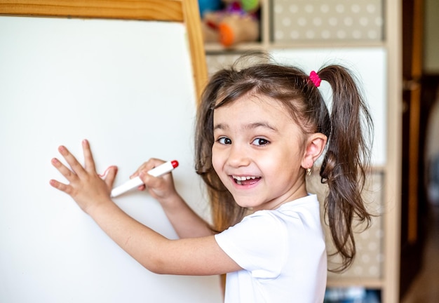 Portrait of a happy little girl who writes with a marker on a modern smart board during class