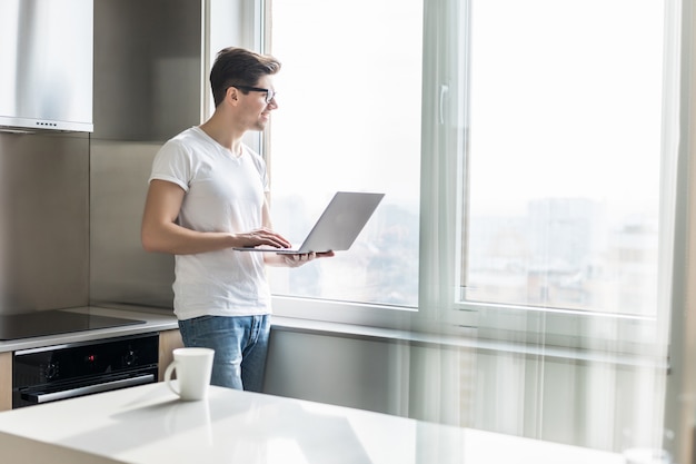 Portrait of happy man holding coffee cup and laptop in kitchen at home. Working from home in quarantine lockdown. Social distancing Self Isolation